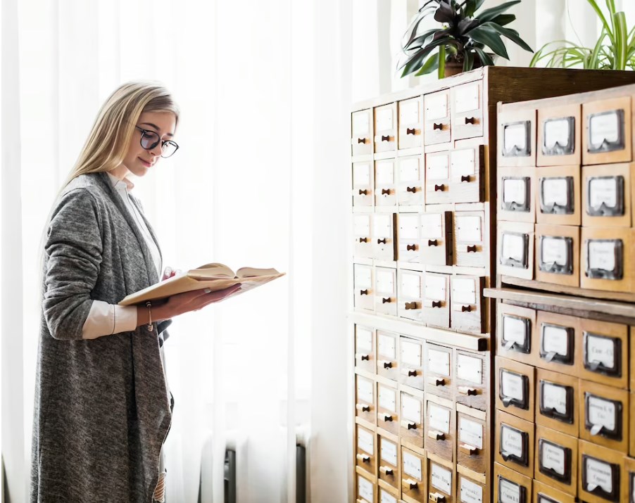 a young lady in glasses reading a book near library document storage folders