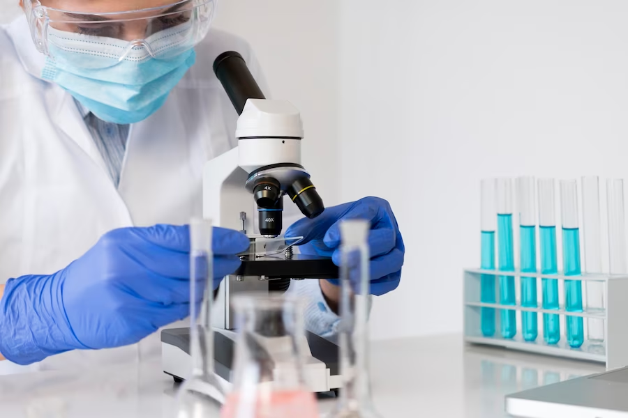 Person in lab gown observing a microscope