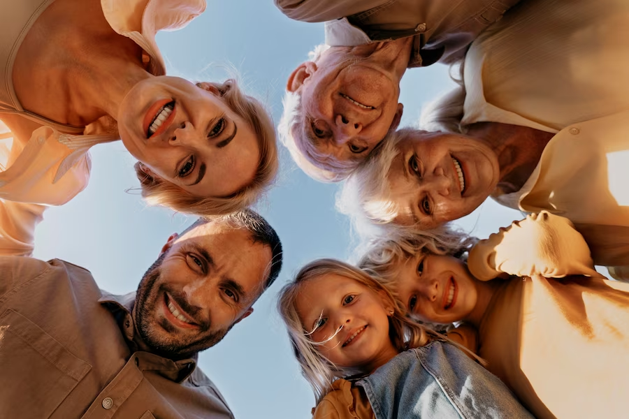 Smiling people of all ages in a circle, smiling and looking down at the camera from below