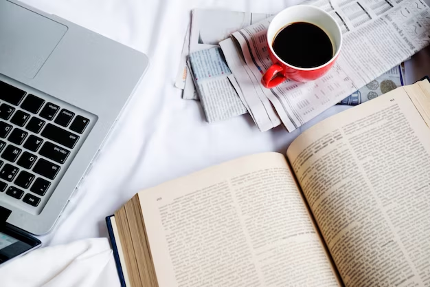 A laptop, book, newspaper, and a cup of coffee together