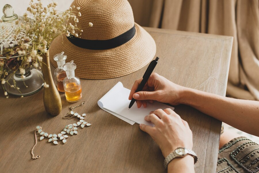 Hand on a table, holding a pen, and writing on a notepad